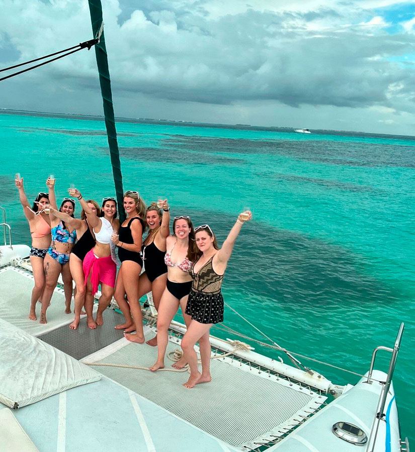 Grupo celebrando en la proa del catamarán sobre agua turquesa
